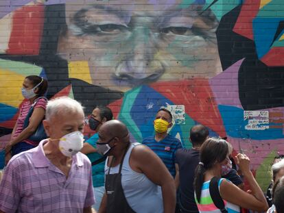 Pedestres caminham diante de mural que retrata o ex-presidente Hugo Chávez em Caracas, em 2 de julho.