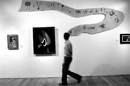 Un hombre camina frente a <i>Friso para la Exposición Internacional del Surrealismo (superstición-serpiente)</i>, de Joan Miró (1947), expuesta junto a obras de Kurt Seligmann y René Magritte.