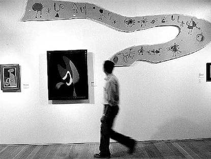 Un hombre camina frente a <i>Friso para la Exposición Internacional del Surrealismo (superstición-serpiente)</i>, de Joan Miró (1947), expuesta junto a obras de Kurt Seligmann y René Magritte.
