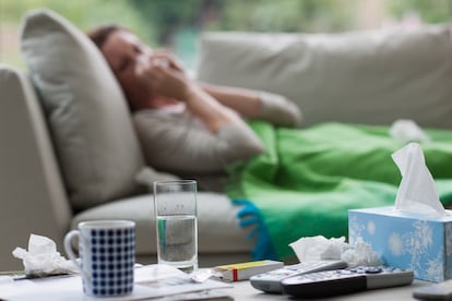 Una mujer afectada por un catarro descansa en el sofá.