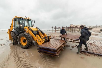 Los propietarios de un chiringuito situado en la playa Cala Bosque, La Zenia, Orihuela, ayudados por una excavadora, retiran las maderas de la pasarela de acceso a la playa.