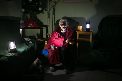 En la imagen, Rosa (73 anos) iluminada con linternas en el salón de su casa durante un corte de luz.