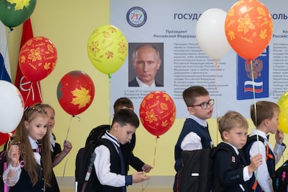 Schoolchildren walk past a poster featuring Russian President Vladimir Putin