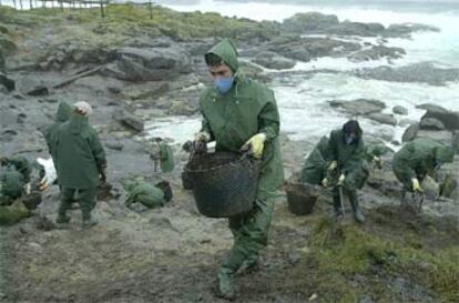 Varios voluntarios recogen restos de fuel en una zona de la costa de la localidad coruñesa de Muxía.