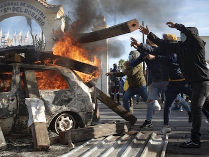 Un grupo de trabajadores lanza vigas de madera a un coche ardiendo.