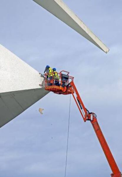 Dos operarios trabajan, desde una plataforma elevadora, en la retirada del revestimiento de la cubierta del Palau de les Arts tras los deprendimientos del pasado mes de diciembre.