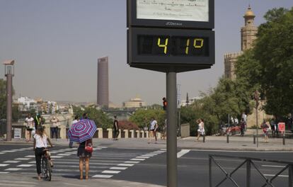 Una mujer se protege del sol con un paraguas mientras espera para cruzar la calle junto a la Torre del Oro en Sevilla, donde la AEMET ha declarado aviso rojo por calor con temperaturas que pueden llegar a los 45 grados.