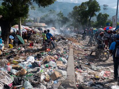 Además, la falta de un servicio de limpia en la mayoría de los barrios de la capital haitiana, ha dejado cientos de calles cubiertas de desperdicios y ha acrecentado la crisis sanitaria. En la imagen, personas circulan por una de las calles cubiertas de basura de Puerto Príncipe, el 8 de octubre de 2022. 