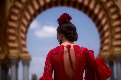 Una joven con traje de flamenca en el recinto ferial delante de la portada de la Feria de Nuestra Señora de la Salud de Córdoba.