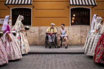 Dos personas observan el desfile de falleras durante la Ofrenda a la Virgen. Los alrededores de la plaza de la Virgen estaban blindados de vallas y de policía para evitar que el público se acercase como otros años.