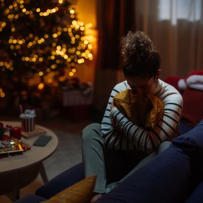 Young woman feeling lonely and depressed during christmas holidays, sitting on the sofa and hugging a pillow