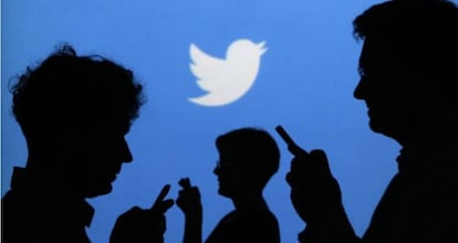 Personas que usan sus m&oacute;viles frente a un cartel de Twitter