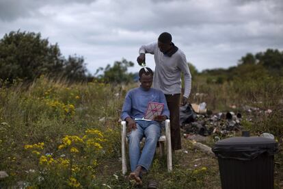 Un inmigrante sudanés corta el pelo a otro de sus compañeros en el campamento que han levantado cerca de la localidad francesa de Calais, donde esperan para intentar llegar a Reino Unido cruzando el túnel del Canal de La Mancha.