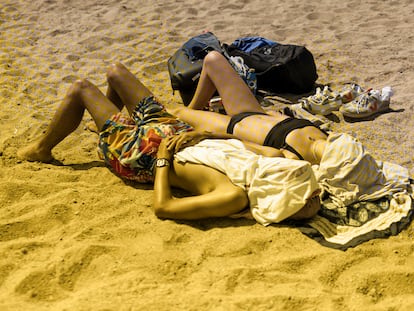 A couple sunbathes on a beach in Barcelona, Spain.