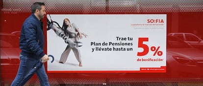 Una persona pasa delante de un cartel promocionando planes de pensiones, en una sucursal de Banco Santander.