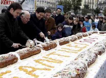 Varias personas cortan el roscón de Reyes gigante que se ha degustado hoy en la Puerta del Sol de Madrid.