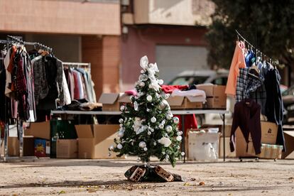 Un pequeño árbol de Navidad permanece en el centro de un plaza junto a la calle Maestro Serrano de Paiporta junto a la ropa que ha traído un grupo de voluntarios.