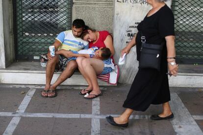Una familia pide limosna a la puerta de un comercio cerrado en Atenas.
