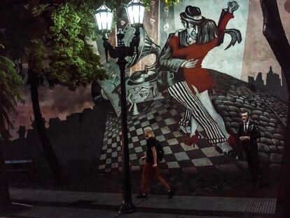 Un hombre pasa por una escena de baile de tango en un mural con una estatua de Roberto Goyeneche, un famoso artista de tango de una época pasada en el barrio de San Telmo, en Buenos Aires (Argentina).