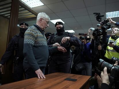 A police officer places handcuffs on Memorial activist Oleg Orlov during a court hearing in Moscow on February 27.