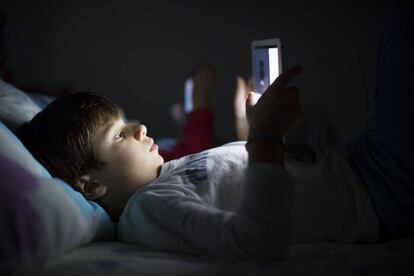 Un niño, tumbado en la cama, utiliza una tableta.