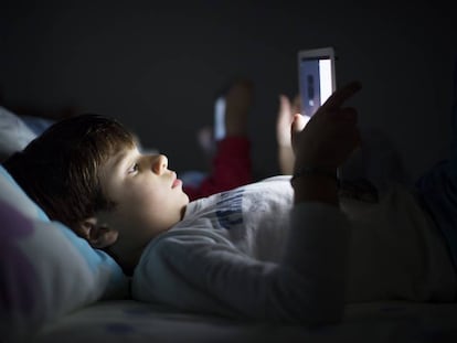 Un niño, tumbado en la cama, utiliza una tableta.