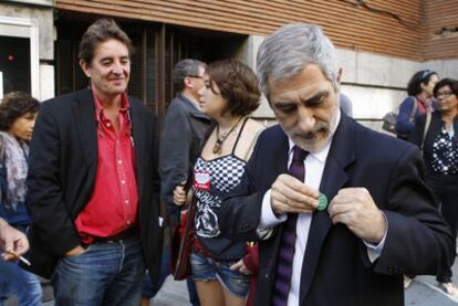Gaspar Llamazares se coloca una chapa verde de apoyo a los profesores de la escuela pública, ayer junto a la sede de CC OO en Madrid. Detrás de él, a la izquierda, el escritor Luis García Montero.