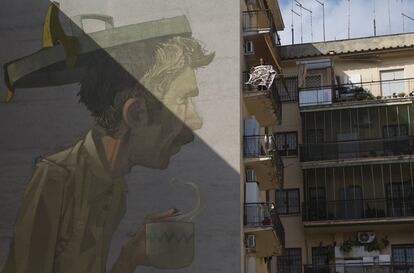 Una mujer sacude una alfombra junto a un mural pintado por el artista 'Etam Cru' en la ciudad de Roma (Italia).