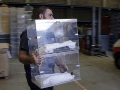 Un operario de la empresa encargada de repartir el material electoral trasnporta una urna en el almac&eacute;n municipal de Barcelona.