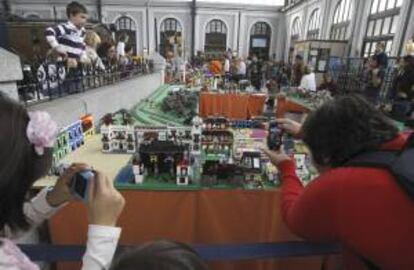 Dos personas fotografían hoy, en el Museo del Tren de Madrid, una exposición con réplicas de trenes, paisajes y pasajeros construidos con piezas de LEGO, que incluye una recreación a escala de la madrileña estación Príncipe Pío, compuesta por más de 18.000 piezas de este popular juego infantil.