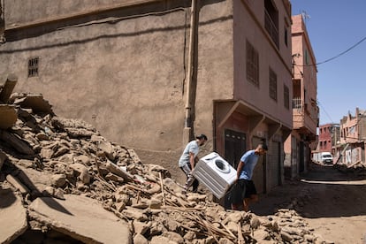 Dos hombres transportan una lavadora por una calle llena de escombros, en Amizmiz. 