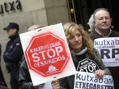 Miembros de Kaleratzeak Stop Desahucios e IRPH-STOP de Gipuzkoa participan en una concentración frente a la sede de Kutxabank en San Sebastián.