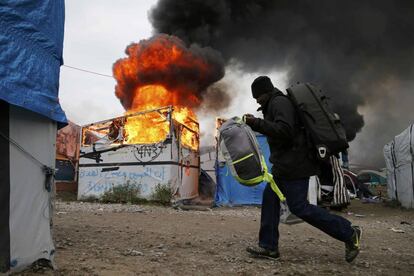 Un migrante transporta sus pertenencias a través de una zona en llamas en el campamento de Calais.