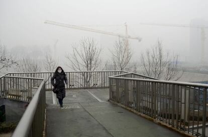 Una mujer con m&aacute;scara cruza un puente de Pek&iacute;n.