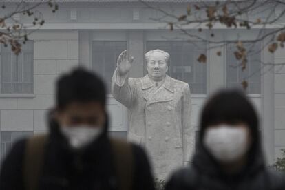 Una pareja con mascarillas frente a la estatua del difunto líder chino Mao Zedong en una universidad, en el centro de Shanghai.