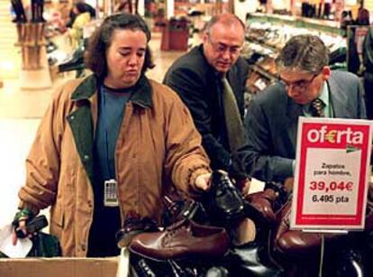 Un grupo de clientes de unos grandes almacenes observan zapatos rebajados en un mostrador.