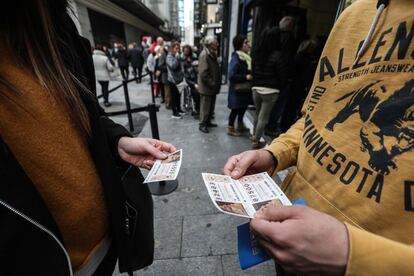 Dos personas estudian sus décimos para el sorteo de el Niño en la calle del Carmen de Madrid, delante de la cola de Doña Manolita, que en el pasado sorteo de Navidad repartió el Gordo y el segundo premio.