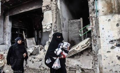 Un par de mujeres caminan con sus hijos frente a un edificio en ruinas de la ciudad siria de Raqa.
