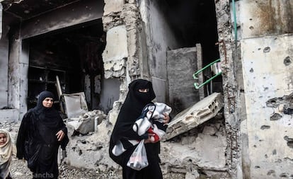 Un par de mujeres caminan con sus hijos frente a un edificio en ruinas de la ciudad siria de Raqa.  