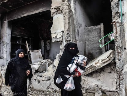 Un par de mujeres caminan con sus hijos frente a un edificio en ruinas de la ciudad siria de Raqa.  