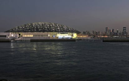 Vista nocturna del Louvre de Abu Dabi con los rascacielos de la capital emiratí al fondo.