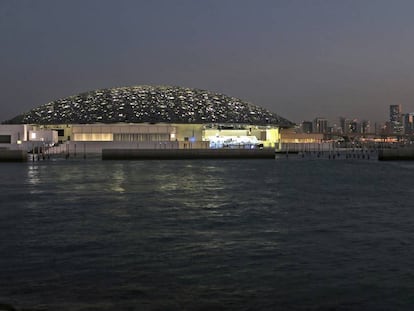 Vista nocturna del Louvre de Abu Dabi con los rascacielos de la capital emiratí al fondo.