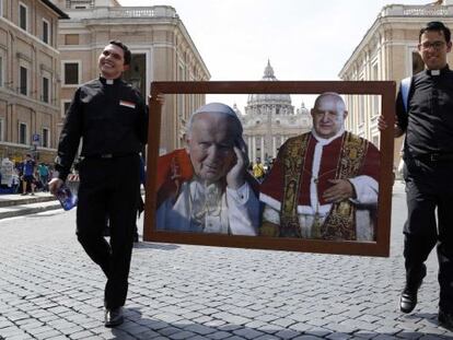 Dos sacerdotes caminan por la Plaza de San Pedro con un collage de los dos papas que serán canonizados el 27 de abril de 2014.