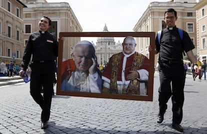 Dos sacerdotes caminan por la Plaza de San Pedro con un collage de los dos papas que serán canonizados el 27 de abril de 2014.