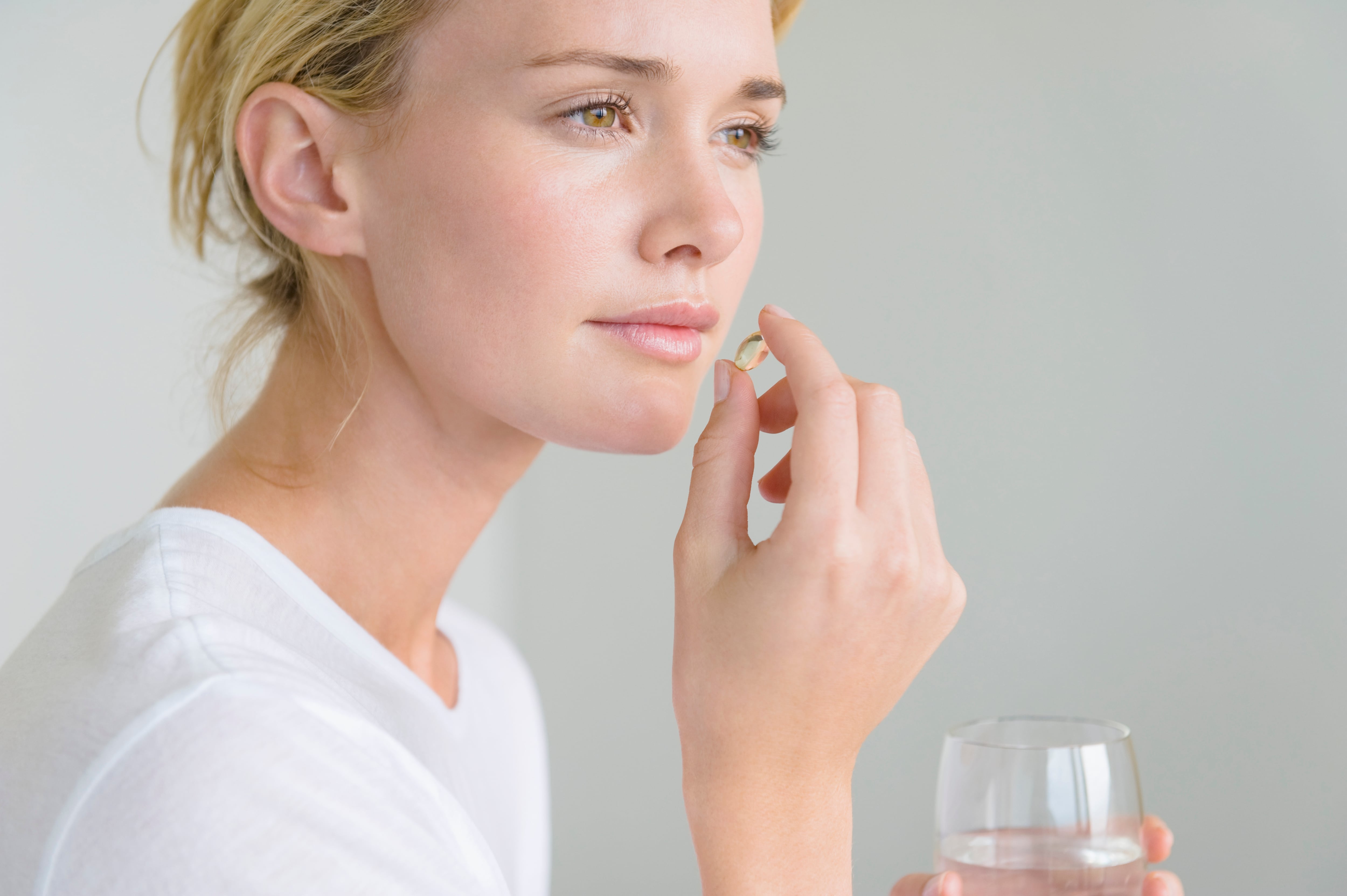 Una mujer blanca con el cutis perfecto toma una cápsula de Omega-3.