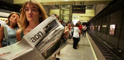 Una mujer lee el periódico ADN en el andén metro de Valencia