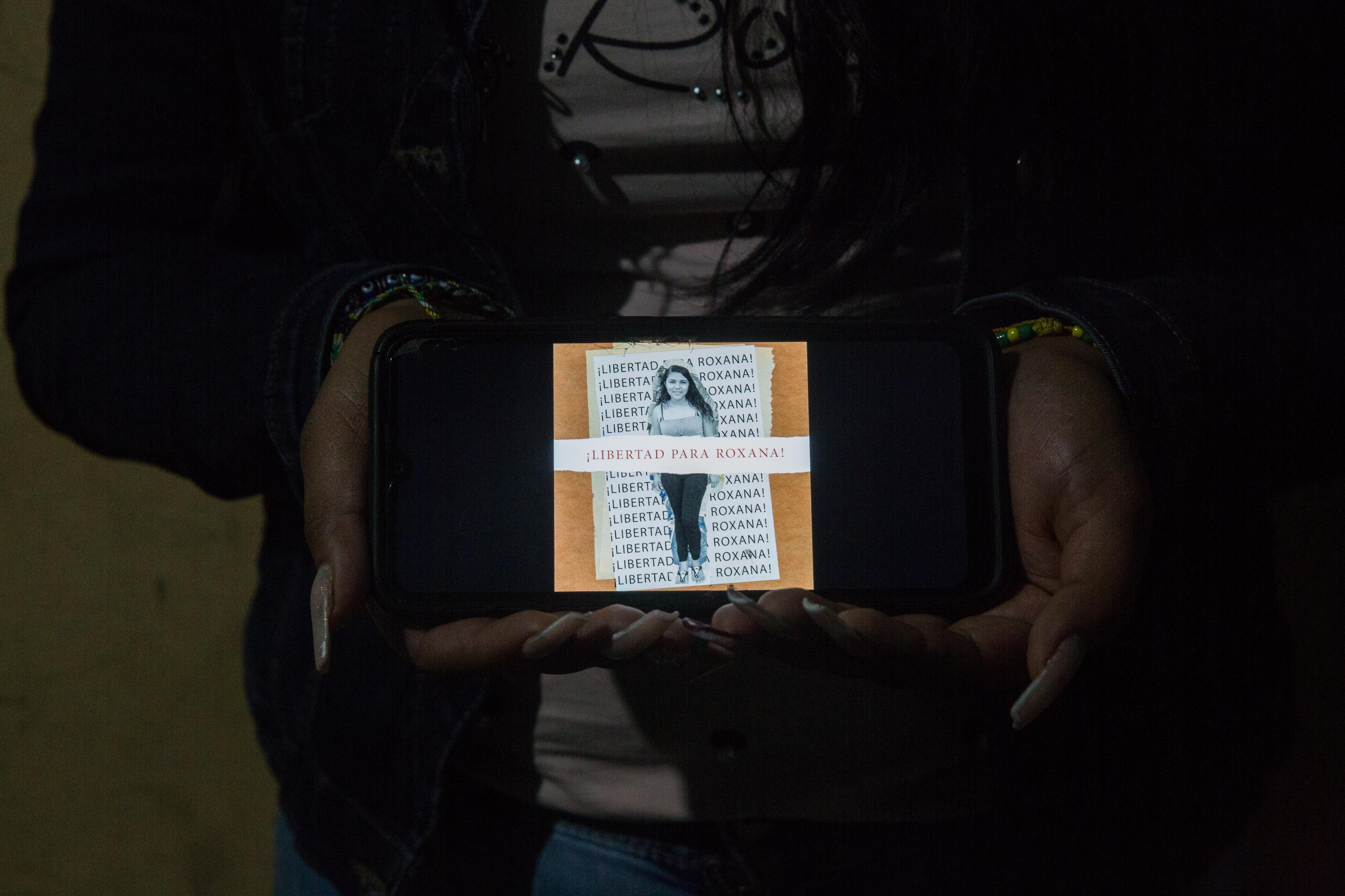 Una mujer sostiene un celular con la imagen de Roxana Ruiz.