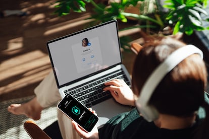 Over the shoulder view of young woman using smart phone while logging in personal banking account on laptop. Network security, data protection and privacy.