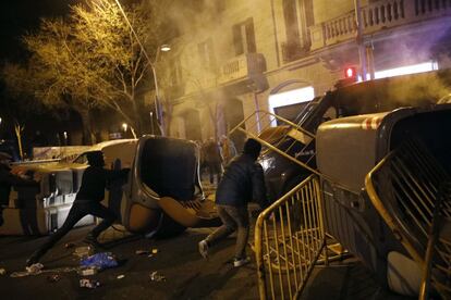 Protesters push garbage containers and metal barriers against a police vehicle.