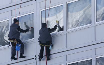 Unos trabajadores limpian los cristales de las ventanas de uno de los pabellones del parque Olímpico.